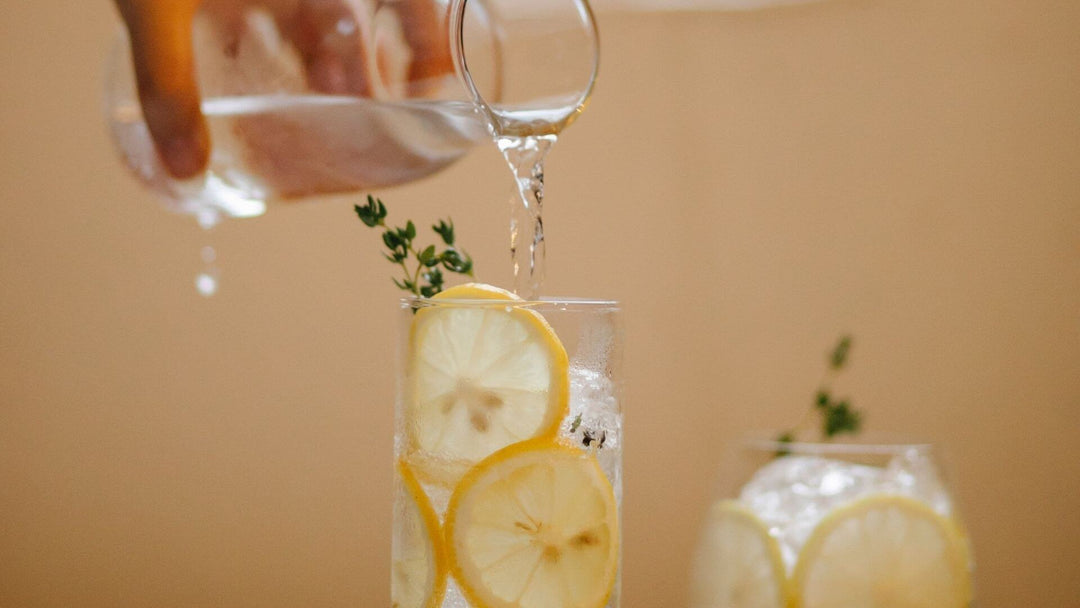 Glass pouring CBD Water with lemons in a glass with a pitcher of CBD Water in the background