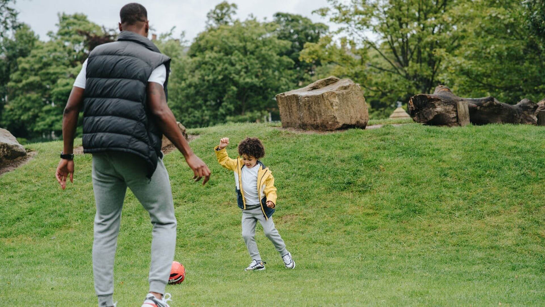 Man kicking a ball with his son, playing in a green grass field